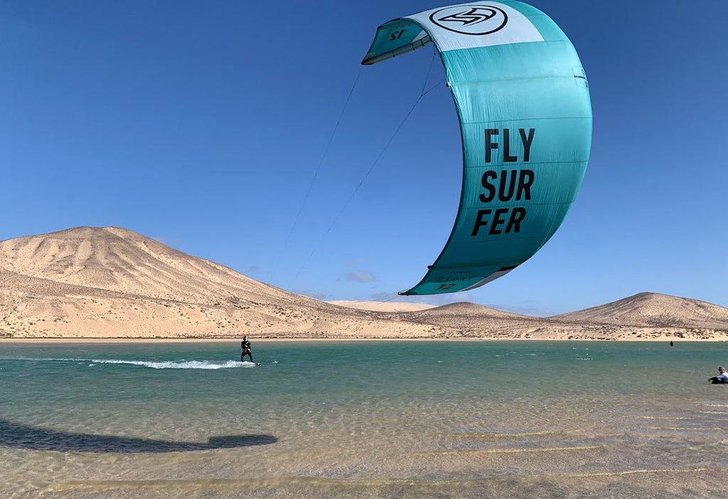 Kitesurfer gliding across the Risco del Paso lagoon with Flysurfer kite and desert hills in the background, Fuerteventura