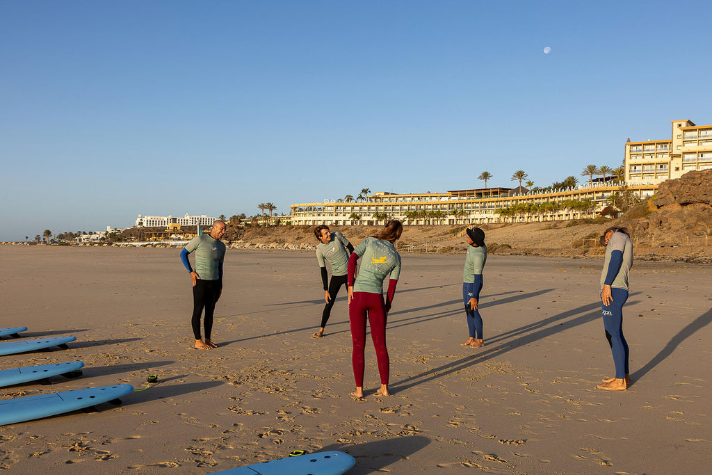 Surfers Island students warming up on the beach in Esquinzo, Fuerteventura before a beginner surf lesson
