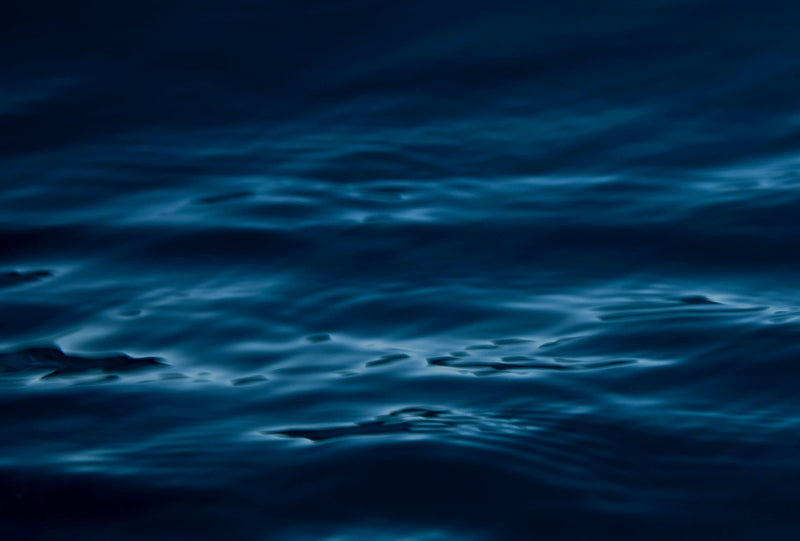 Calm dark-blue ocean surface with soft ripples and reflections, captured during twilight. Abstract marine texture.