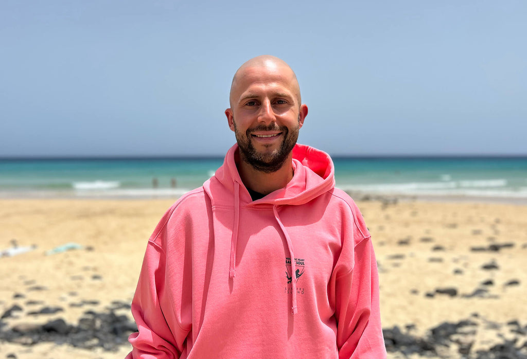 Surf-, Kitesurfinstructor Sander in front of the Surfers Island Station at the beach of Morro Jable wearing Surfers Island Hoodie Merch